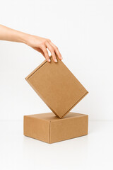 A woman's hand carefully places a small brown cardboard box on top of another against a white background.