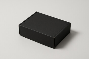 A simple closed black rectangular cardboard box resting on a plain light gray surface.