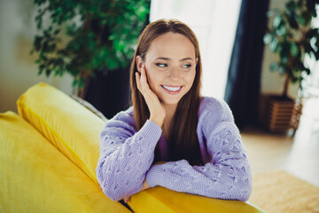 Obraz premium Young brunette woman relaxing at home on a yellow sofa in a lavender sweater smiling and enjoying leisure time