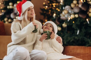 Green cups of tea are in hands. Mother and daughter are celebrating New Year at home in domestic...