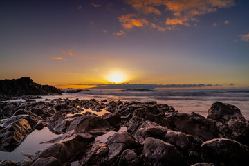 Sunset over volcanic rocks on Tenerife&rsquo;s coast. Warm golden light reflects in tide pools as waves roll gently in, creating a peaceful and dramatic seascape.