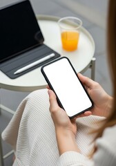 Woman using a blank screen smartphone with a tablet and orange juice on a table for mockup and app promotion in a bright and modern setting