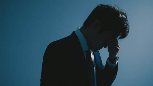 株価の下落に悩み頭を抱える男性の横向きシルエット