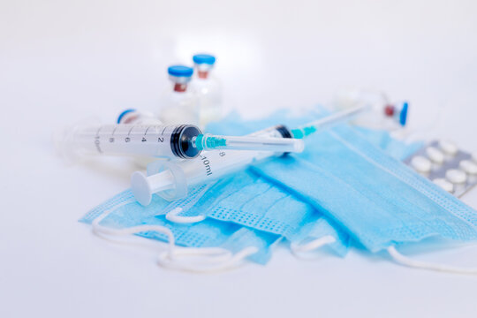 A still life of medical syringes and medication vials. Disposable syringes, medical masks, and fever pills. Supplies for injections and virus protection. 