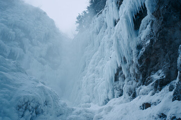 Frozen waterfall with icicle formations, blue-white winter tones, misty cold atmosphere, cinematic nature scene