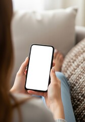 Woman relaxing at home using a smartphone with a blank white screen for app design and mobile content creation on a comfortable sofa in a cozy living room
