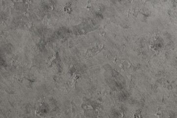 A close-up of a rough, uneven gray textured surface. It shows subtle tonal variations and visible, irregular trowel marks, giving it a distressed, industrial feel