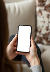 Woman holding a smartphone with a blank white screen while relaxing on a sofa in a cozy home setting offering space for mobile app advertising
