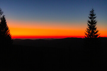 Brilliant band of sunset color stretching across a mountain horizon, vivid orange melting into cool...