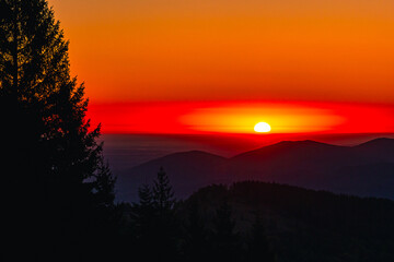 Sunset bathes layered mountains in the vivid orange red glow. Dark spruce silhouettes edge the frame, adding depth and calm. Perfect for travel ads wellness brand, prints, and calm web banners.