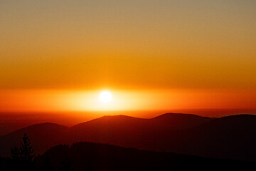 Soft sunrise over layered mountain ranges and a warm orange horizon. Hazy, calm, minimal, this soothing landscape captures quiet morning light, perfect for travel, wellness content, posters. Ads.