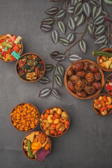 A variety of nuts and dried fruits are displayed in bowls on a grey background.