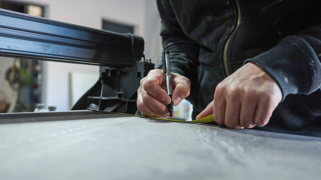 A person's hands measuring and marking a surface with a pen and tape measure