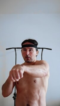 A man mastering reflex boxing drill, casual home session with red elastic ball, orange shorts, headband, quick hand movements and playful intensity, focus on reaction timing and technique