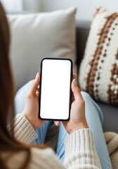 Woman holding smartphone with blank white screen while relaxing on sofa at home offering mockup space for apps and mobile content perfect for advertising use