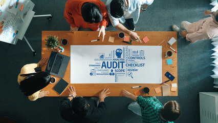 A diverse group of professionals collaborates around a wooden conference table, focusing on an audit checklist, with notes and documents scattered in an engaging workspace. Amity