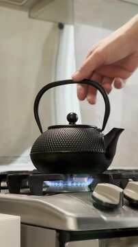 Iron teapot heating on a stovetop with hot tea inside, steam rising gently.