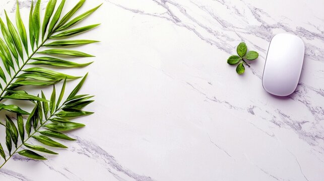 A white computer mouse and green leaves are arranged on a white marble surface, creating a clean and minimalist composition.