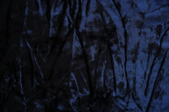 Dark blue velour fabric texture, close-up plush surface and natural folds. The detailed texture shows characteristic light reflections and smooth, velvety appearance typical for velour used in clothin