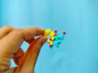 hand holding yellow pill with colorful medicines in the background