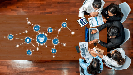 A top-down view of a diverse business team engaged in a project discussion, utilizing technology tools and data visualization graphics in a modern office environment. Amity