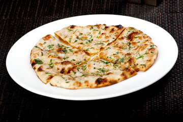 Freshly baked Indian flatbread (Naan or Kulcha) cut into quarters, topped with fresh cilantro and butter/ghee, served on a white plate. Perfect accompaniment to curry dishes.