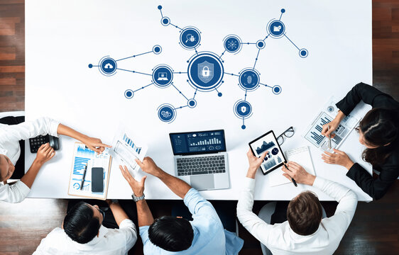 A diverse team engages in a meeting focused on data security, utilizing various digital devices and discussing infographics in a modern workspace. Amity - Powered by Adobe