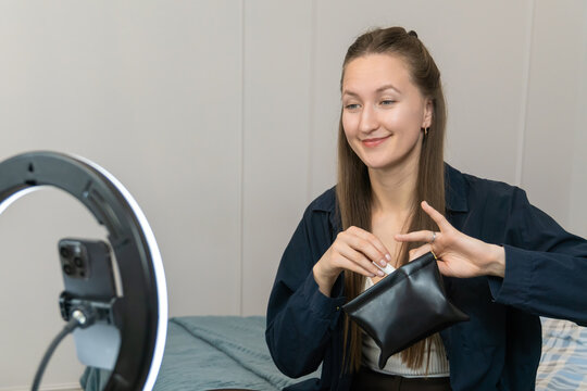 Beauty blogger engaging followers by presenting makeup products during a live stream, utilizing a smartphone and ring lamp to create captivating content in a home studio setting - Powered by Adobe