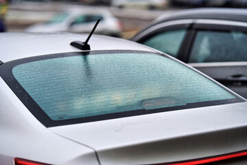 Closeup view of car rear window covered in frozen water droplets after freezing rain, icy textured surface and significantly reducing visibility during harsh winter weather conditions. Selective focus