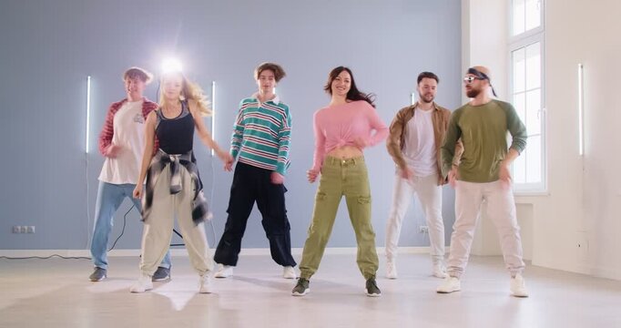 Cheerful group of young people dancing together in dance studio. Men and women in casual clothes learning new energetic dance movements together. Active lifestyle and sport concept. 4k video.