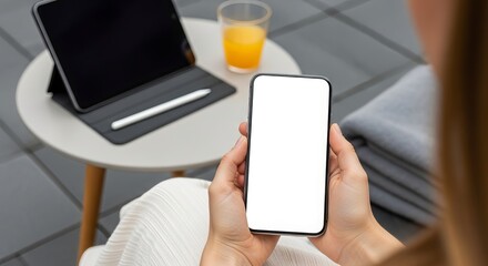 Woman holding smartphone with blank screen near tablet and orange juice on a modern table showcasing mobile technology and lifestyle integration