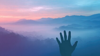 Silhouetted hand reaching towards a misty mountain range at sunrise
