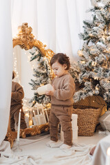 Little boy playing near Christmas tree with presents and electric candles. 
