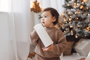 Little boy playing near Christmas tree with presents and electric candles.