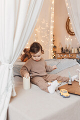 Little boy sitting on the bed in front of christmas tree. Toddler playing with toys and candles. Brown colors.