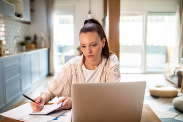 Young adult woman stressed paying bills at home kitchen table