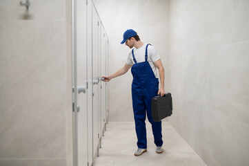 Plumber checking toilet cubicle door holding toolbox