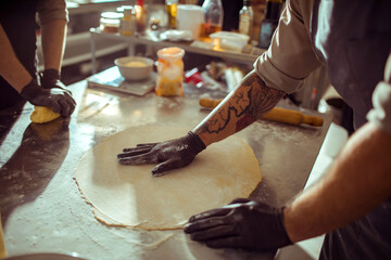 Adult chefs kneading dough focused in professional kitchen