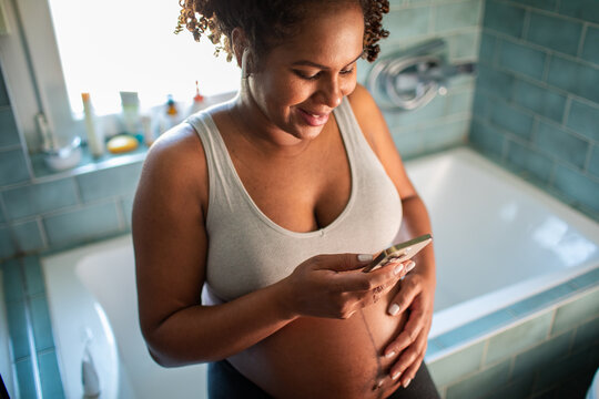 Adult pregnant woman smiling while texting in home bathroom