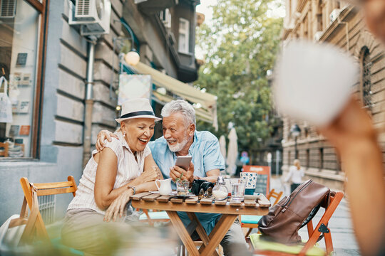 Senior couple laughing at smartphone in outdoor street cafe