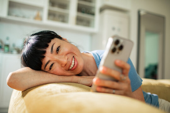 Young adult woman smiling and relaxing with smartphone at home - Powered by Adobe