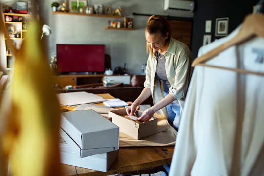 Young adult woman packing online orders at home, focused and content