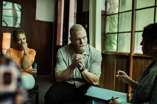 Adult man listening anxiously during group therapy at counseling center - Powered by Adobe