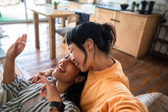 Adult lesbian couple laughing and cuddling on sofa at home