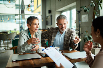 Mature couple discussing finances with advisor in cafe, engaged