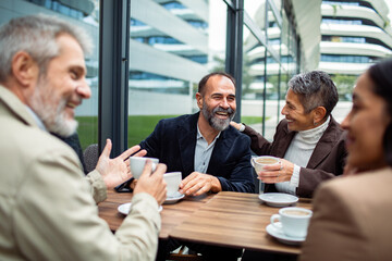 Mature colleagues laughing happily over coffee at outdoor cafe