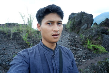 Candid Portrait of Young Asian Man Outdoors at Rocky Volcanic Terrain
