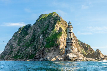 Aniva former japanese lighthouse photographed from sea. Abandoned tower stands at base of steep...