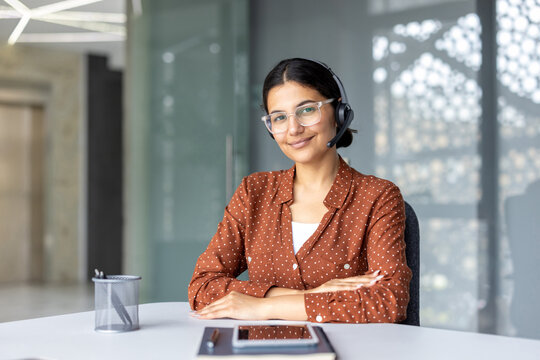 Young professional woman providing diligent customer support, working at a modern call center desk while wearing a headset and looking directly at the viewer