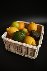 Organic lemons, limes, oranges and avocados placed in a white wicker basket. Fresh natural ingredients for healthy eating, cooking, wellness and immunity-related themes.